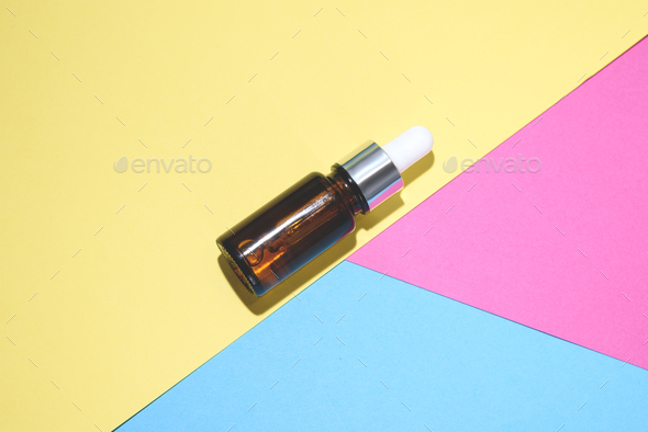 A cosmetic jar with glass dropper on the multi colored background.