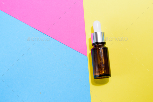 A cosmetic jar with glass dropper on the multi colored background.