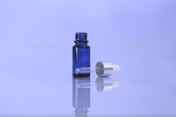 A cosmetic jar with glass dropper on the blue background.