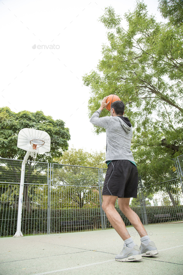 Vertical photo of a man throwing a ball on an outdoor basketball court