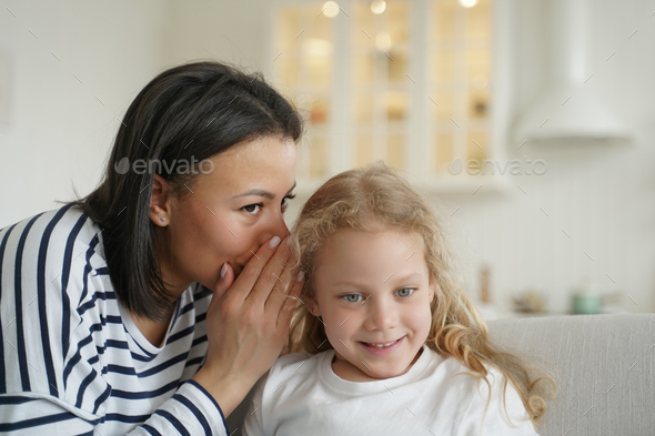 Mom or babysitter whisper secret to little elementary kid girl daughter. Family unity, child care