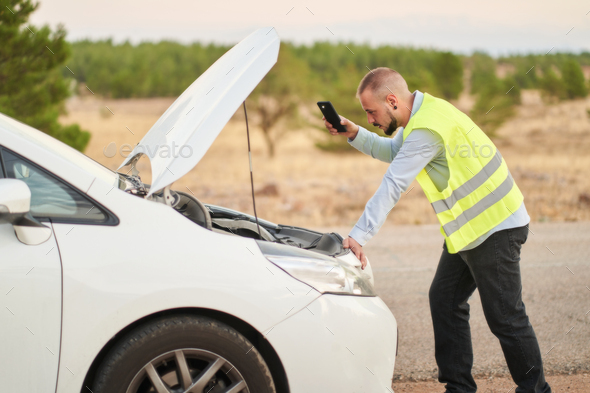 a man looking at the engine of his car wearing an emergency vest because it has broken down
