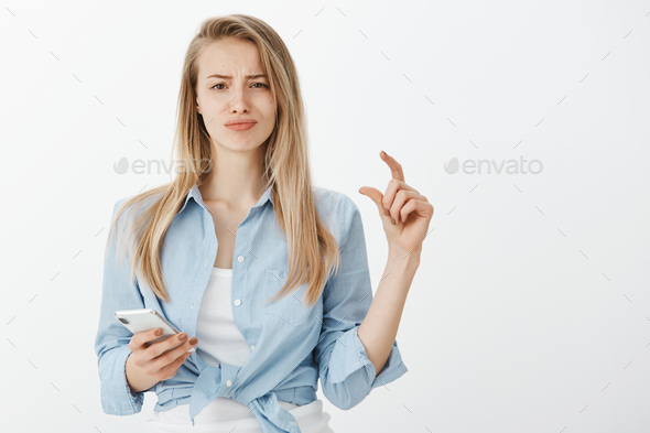 Portrat of unimpressed unhappy european woman with fair hair, shaping tiny or small thing with finge