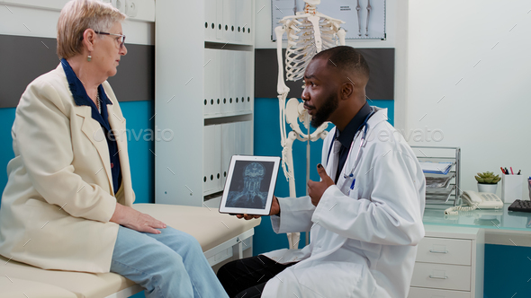 Health specialist analyzing x ray scan on digital tablet with senior patient
