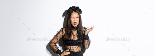 Frustrated and angry young asian woman in witch dress arguing with someone, looking pissed-off and