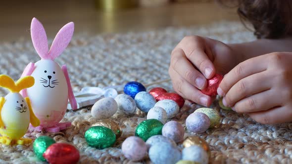 Girl draws a pattern on an Easter egg next to an egg in the shape of a rabbit