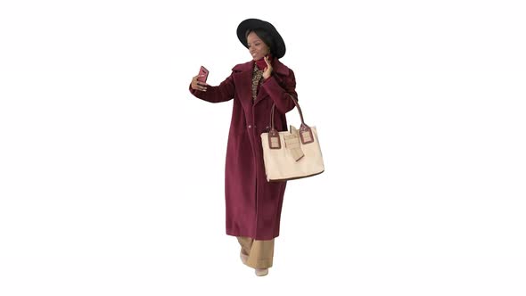 Beautiful African American Fashion Girl in Coat and Black Hat Texting on Her Phone While Walking on alt