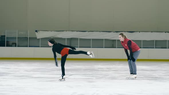 Figure skating girl doing exercise on ice rink with her trainer