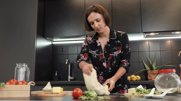Woman kneading dough on wooden table with flour while working in kitchen alt