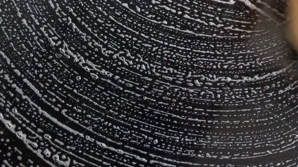 The hands of a man with a sponge washes the stove and other appliances in the kitchen after cooking. alt