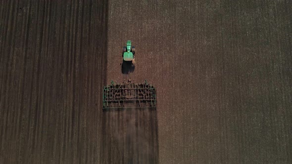 Tractor with harrow system plowing ground on cultivated farm field, agriculture. alt