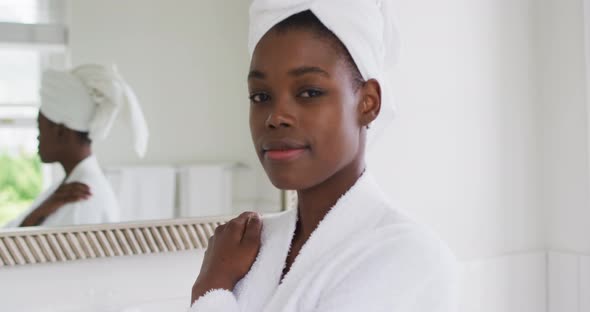 Portrait of african american woman in bathrobe smiling in the bathroom at home alt