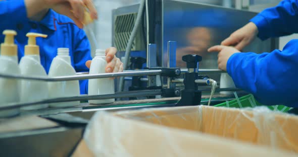 Closeup of a Woman's Hands That Twists the Lids on White Plastic Bottles on a Conveyor Belt of a alt