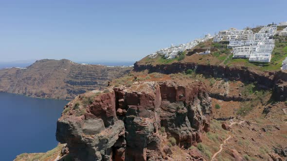 Aerial panning shot of one man standing on Skaros rock in Santorini, Greece alt