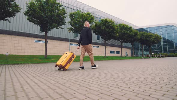 Male Businessman Goes on a Business Trip. A Man Goes To the Airport Holding Luggage in His Hand. alt