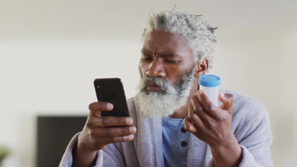 Senior man using smartphone while holding empty medication container alt