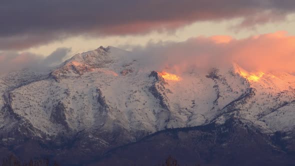 Panning view of snow covered mountain peaks lit up at sunrise alt