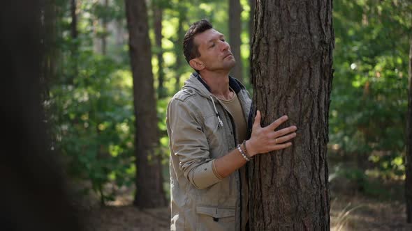 Caucasian Man Admiring Tree Trunk Standing in Sunny Spring Summer Forest alt