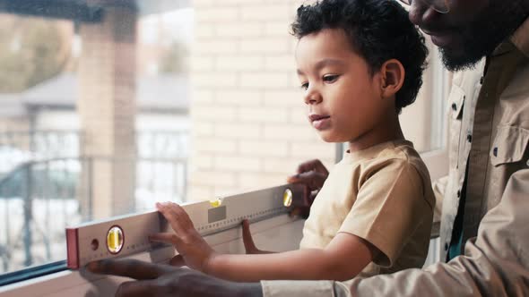 African American father explaining his son how carpenter's level is working