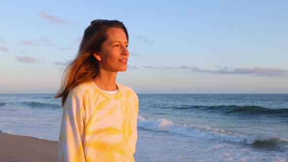 Woman walking along the beach at sunset. alt