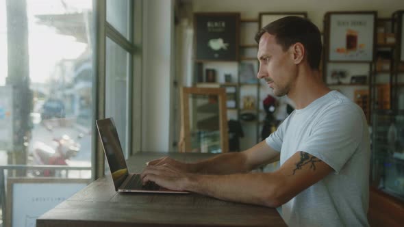 Digital Nomad Works on a Laptop in a Coffee Shop alt