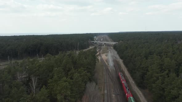 AERIAL: Red and Green Colour Cargo Train Driving on a Railroad under a Bridge