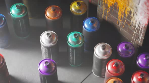 Used, colorful spray paint cans standing in front of a painted brick wall. 4KHD alt