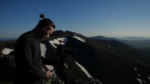 A Male Photographer Stands High in the Mountains Filming Video of the Mountain alt
