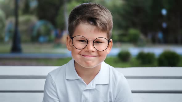 Portrait of Smiling Cute Boy Posing on Bench at City Park alt