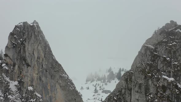Drone flying between high mountain peaks in thick fog and revealing a large cabin in snow covered la alt