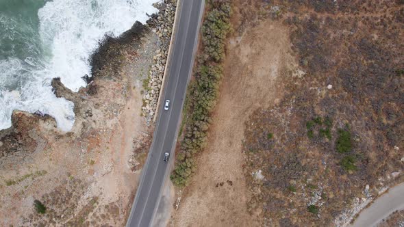 Following cars Aerial top down view from above on the country road between rocks and ocean waves alt