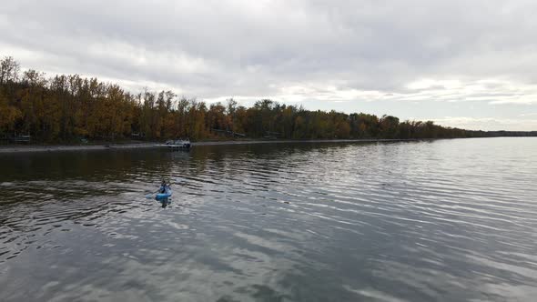 Young woman sitting in a small blue kayak paddling over Buffalo Lake on a cloudy autumn day. Aerial alt