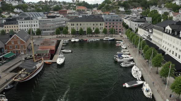 Sailboats And Yachts Anchored On The Pier With The Seaside Town Of Arendal, Norway.  - aerial drone alt
