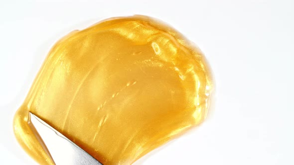 Artist Mixing Gold Paint Using Palette Knife Applied on a White Background alt