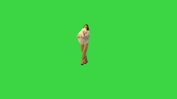 Smiling Glamorous Woman in White Holding White Fluffy Dog While Walking on Camera on a Green Screen