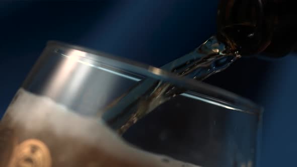 Beer fills up a pilsners glass from a bottle in slow motion. Close up.