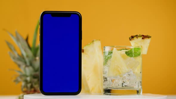 Pineapple Lemonade and Smartphone with Blue Chroma Key Screen on Orange Background alt