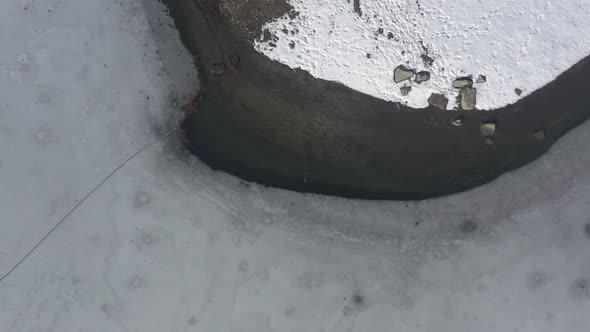 Snow on coast and ice on water surface of lake 4K aerial video alt