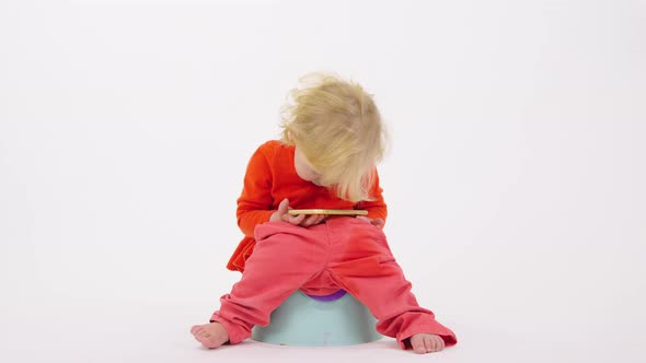 Funny Girl Toddler Sits on Child's Potty Explore Smartphone on White Background