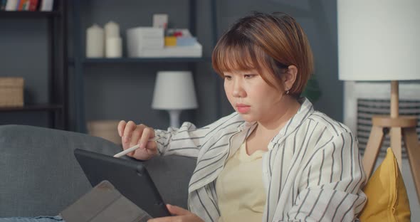 Freelance Asia using tablet online learning in living room at house.