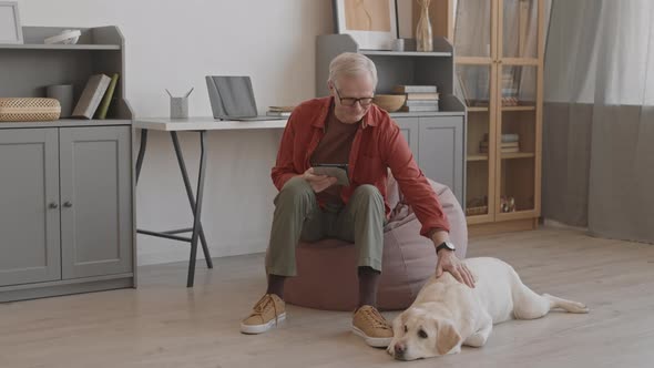 Senior Dog Owner Petting His Pet Lying on Floor at Home alt