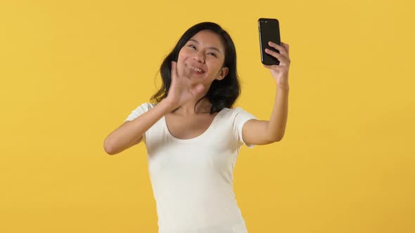 Smiling cute Asian woman taking selfie and waving hand to smartphone