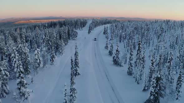 Aerial view above snowy Scandinavia landscape following vehicle on journey along long curved remote alt