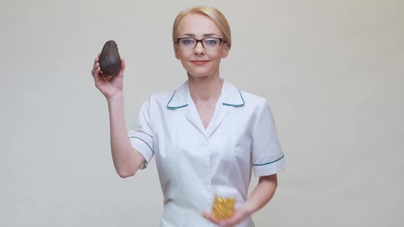 Nutritionist Doctor Holding Organic Avocado Fruit and Jar of Medicine or Vitamin or Omega 3 Capsules alt