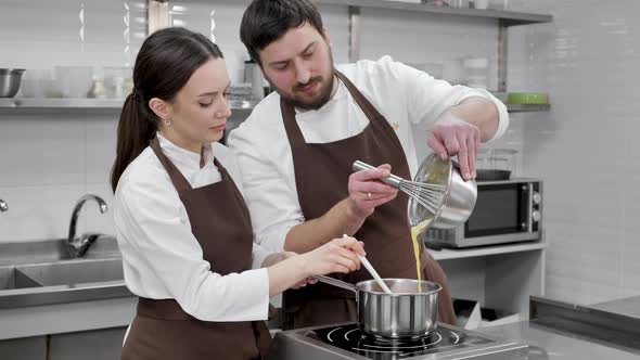 Couple of Confectioners a Man and a Woman Prepare a Mousse in a Professional Kitchen Pour the Yolks alt