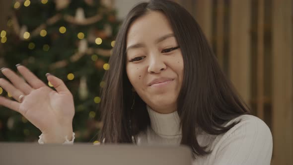 Close Up Asian Woman on a Video Call on Her Laptop with a Christmass Tree on Background Indoors alt