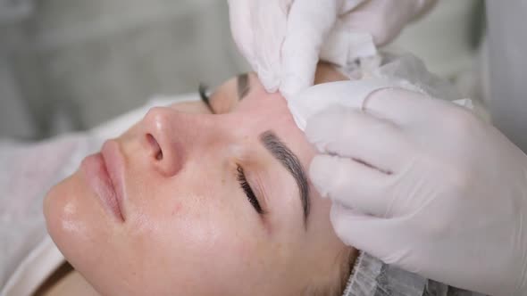 Doctor Beautician in a Black Mask Makes Cleaning the Face of a Young Woman alt