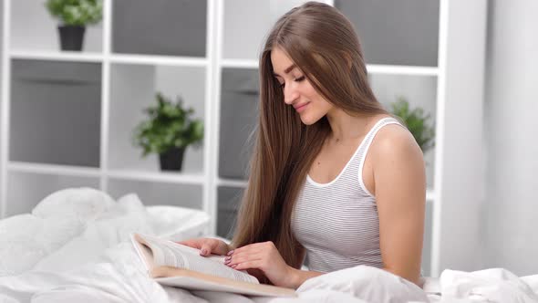 Domestic Beautiful Girl Enjoying Leisure Reading Book Sitting on Bed alt