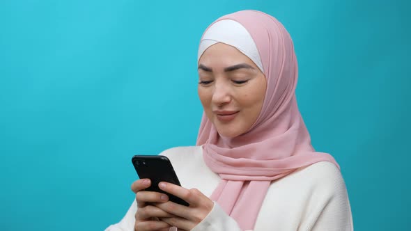 Young Muslim Woman Typing Message on Mobile Phone and Smiling Chatting Having Online Communication