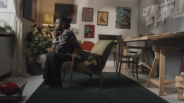Indian Artist Resting in Armchair in Workshop alt